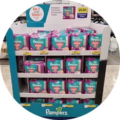 Pampers Premium Protection Pants displayed on a store shelf, featuring a special offer to buy 2 and donate 1 for charity