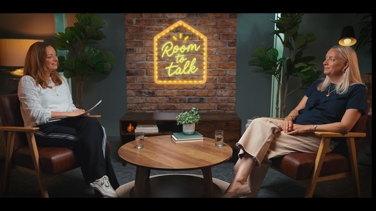 Two people seated in armchairs during a Room to Talk interview.