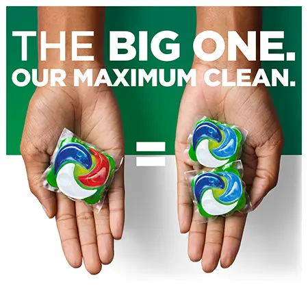 One hand holding a single laundry pod, with two pods shown beside it and an equal sign between them, alongside the text “The Big One. Our maximum clean.”