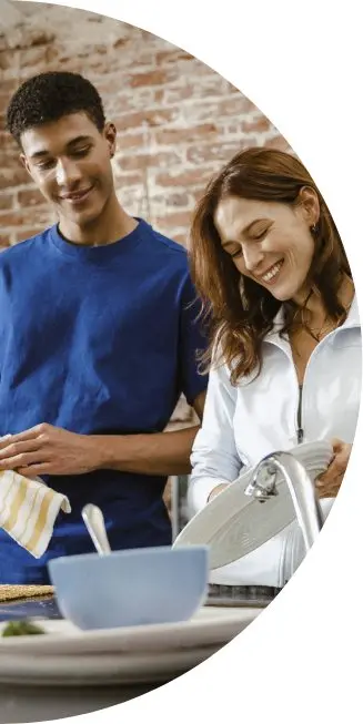A man and woman smile as they wash dishes together
