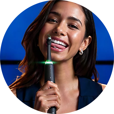 Woman smiling while holding an Oral-B electric toothbrush against a blue background.