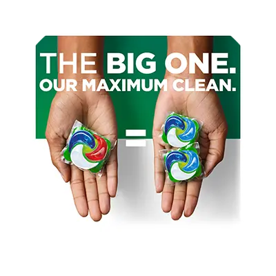 One hand holding a single laundry pod, with two pods shown beside it and an equal sign between them, alongside the text “The Big One. Our maximum clean.”