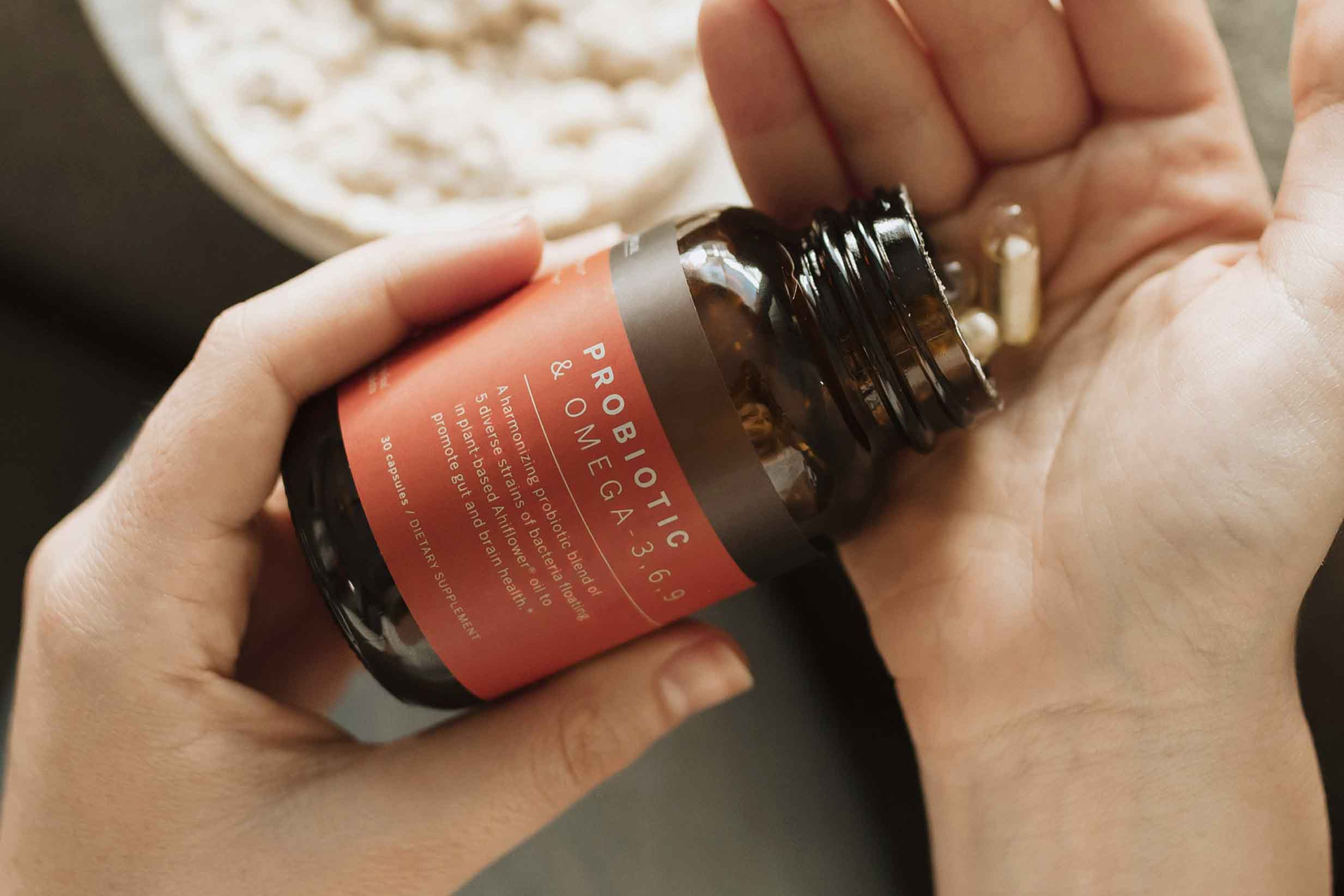 A hand holding a bottle of probiotics, with some capsules falling out into the other hand.