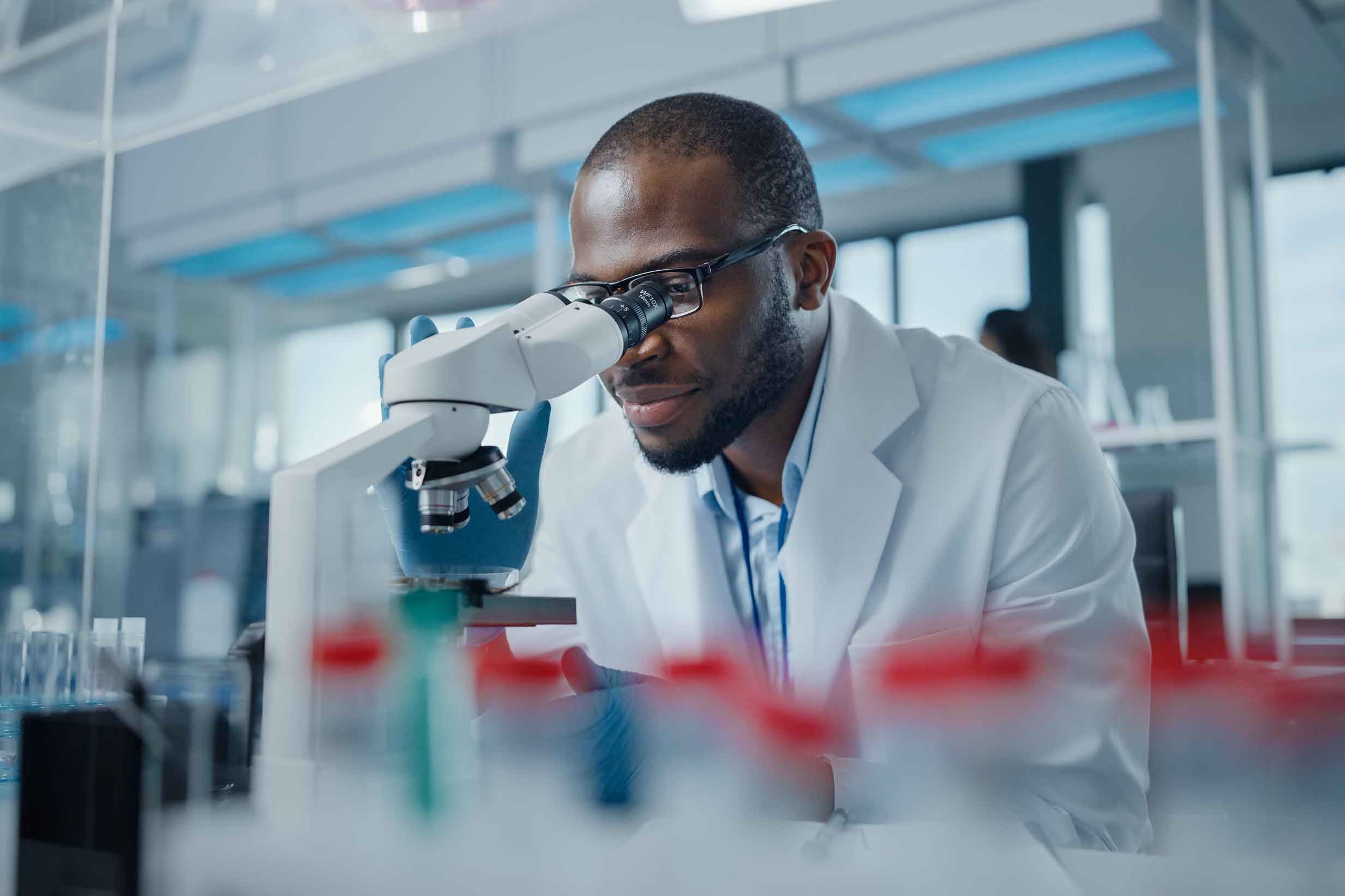 A Black scientist is looking through a microscope.