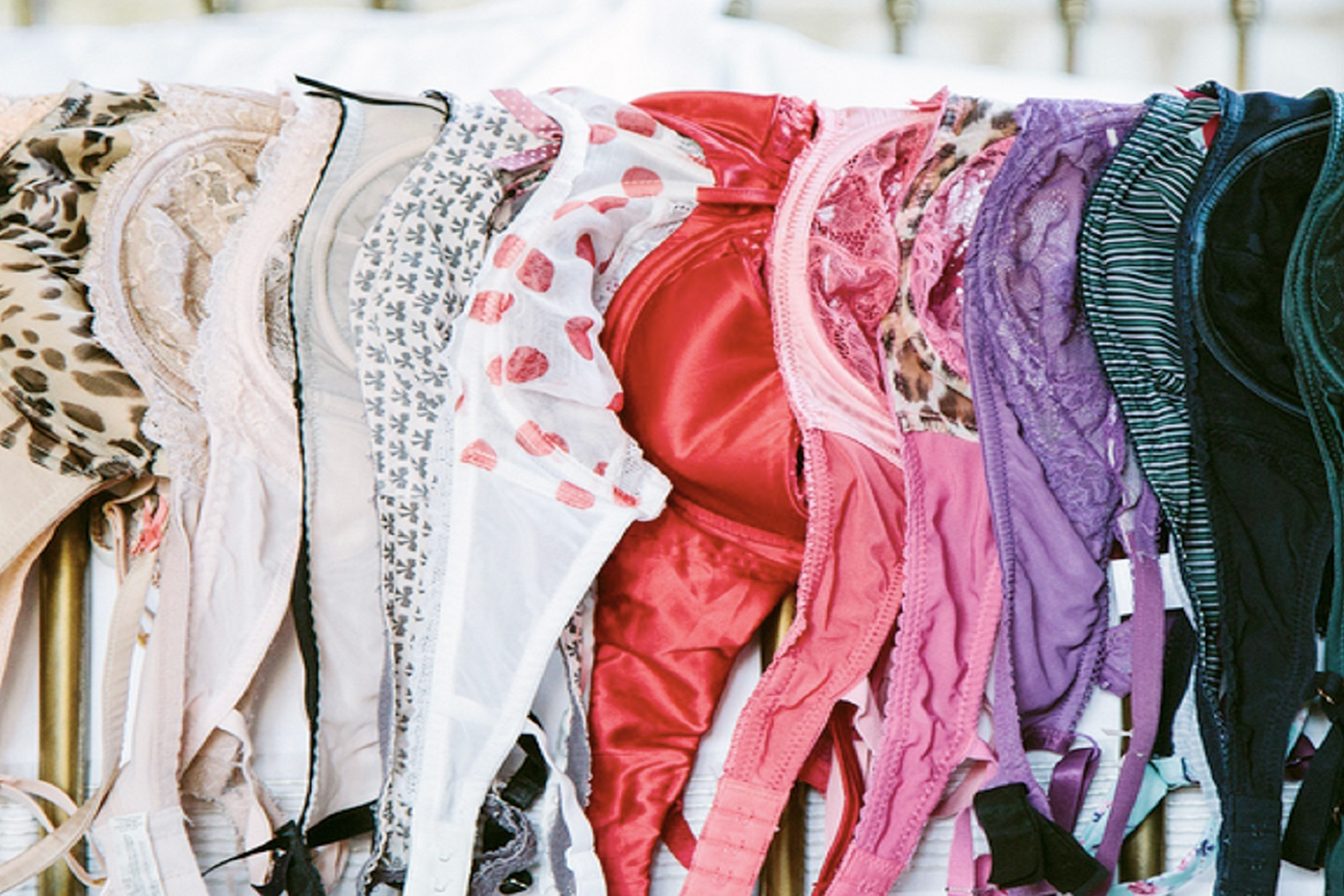 A dozen colorful bras neatly hung up in a row along a rod. 